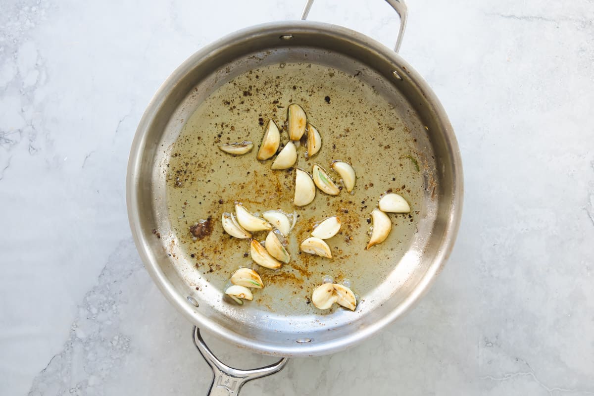 Garlic and herbs cooking in wine in a skillet.